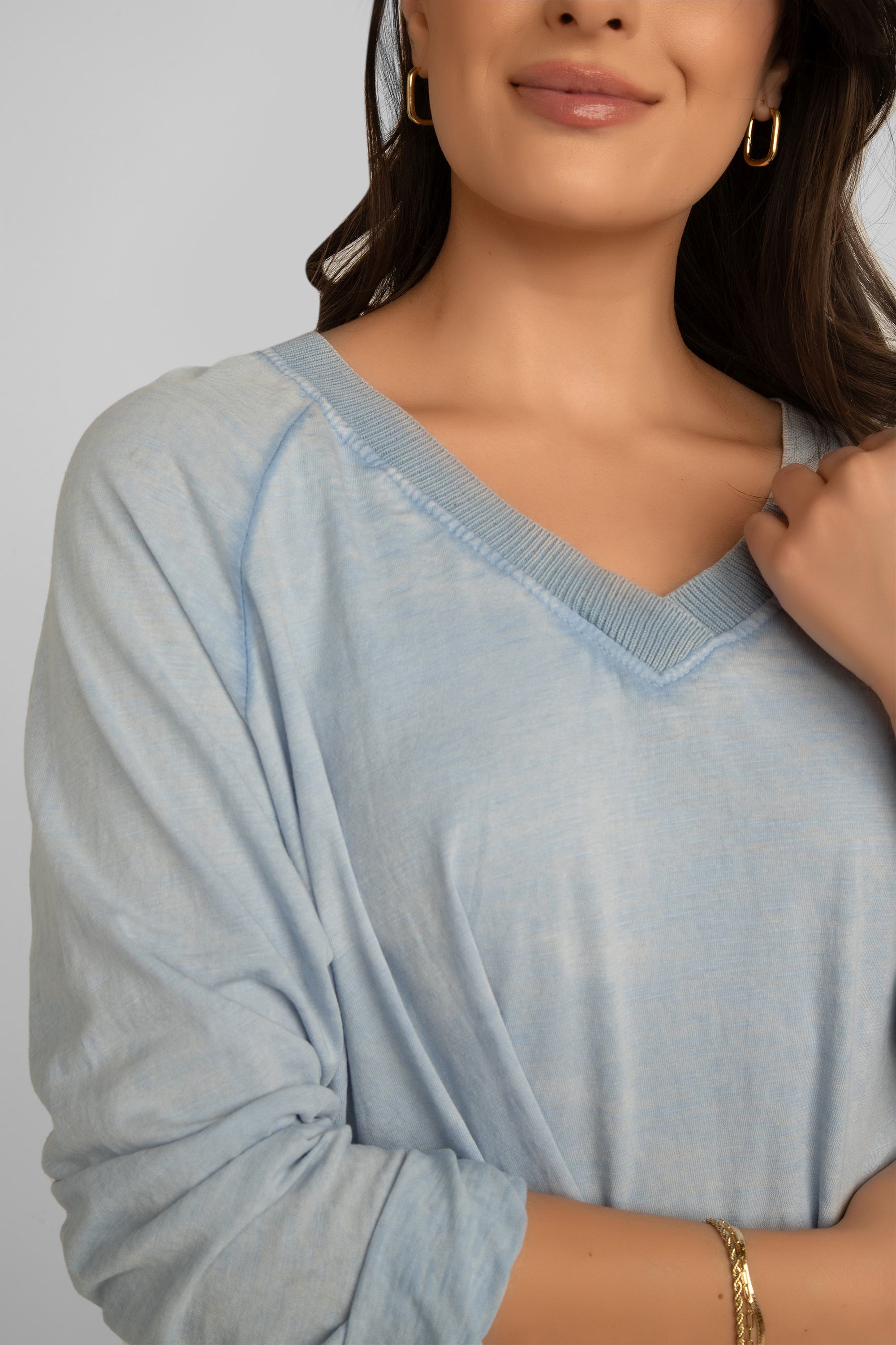 Front close up of garment dye and v-neck on Elissia (JY3734) Women's Long Raglan Sleeve Garment Dye V-Neck Top with Button Patch Detail on left hip, and a high low hem in Baby Blue